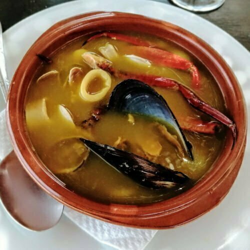 Zarzuela De Mariscos -Spanish Seafood Stew served in an earthenware dish, sitting on top of a white tablecloth