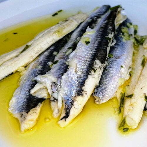 boquerones - Spanish anchovies cured in vinegar and olive oil, served on a plate with some crushed garlic, cilantro, and lots of golden extra-virgin olive oil