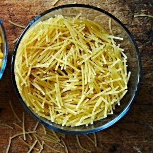 Asmall glass of fideo pasta sits on a rustic chopping board