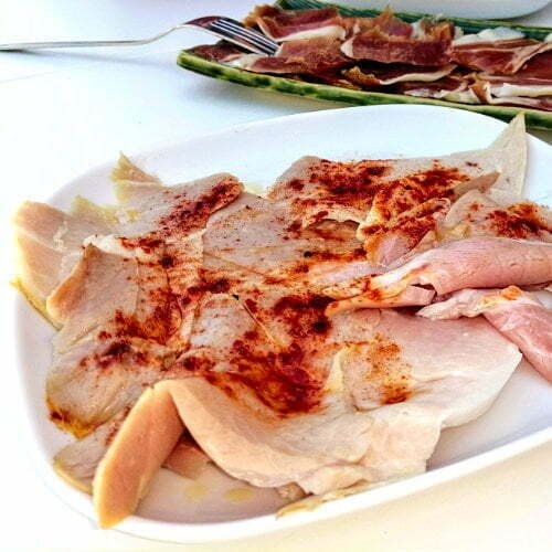 A plate of lacón a la gallega, Spanish ham, served in a bbq table setting with Jamon iberico in the background