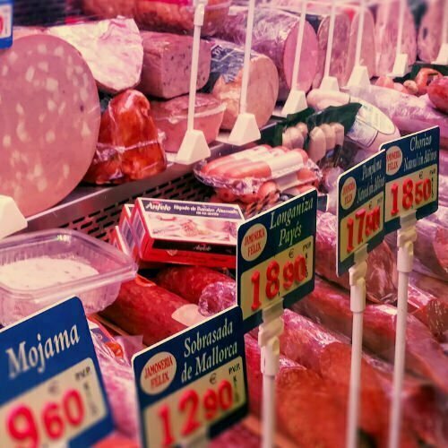 A meat counter displaying many various cuts of meat in a market setting. 