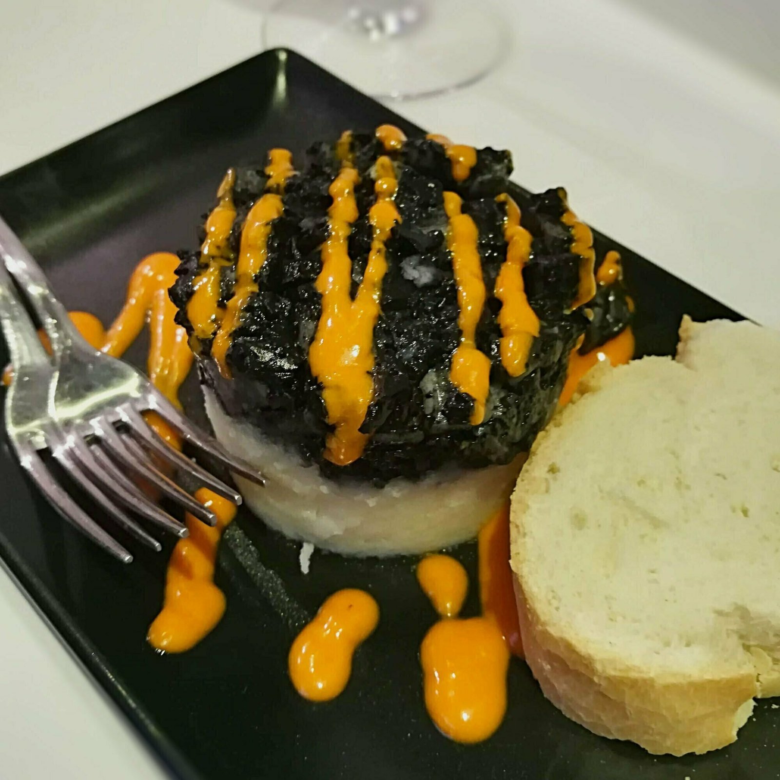 A tapa of morcilla served on a slice of white bread with a spicy sauce.