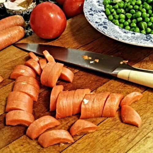 Arros Caldoso ingredients. A large chopping board sits on a kitchen counter with carrots, tomato, and a bowl of peas sitting nearby