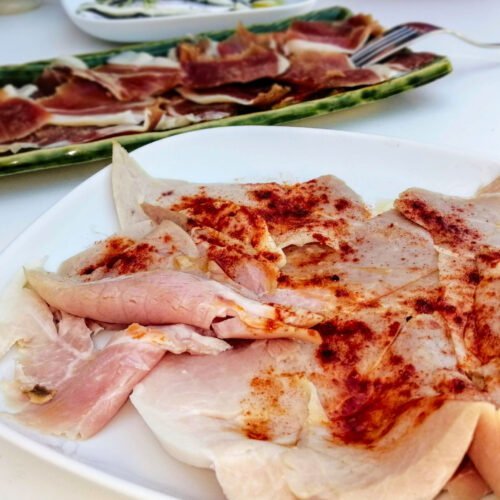 A plate of Lacón a la Gallegasits on a table with a small plate of jamon iberico in the background