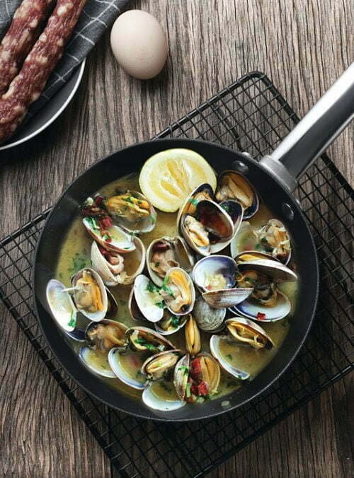 A large pan of cooked clams sits on a wooden benchtop
