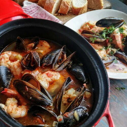 A large red pot filled with Spanish Seafood Stew, brimming with mussels, prawns, and fish.