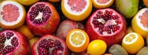 Pomegranites, lemons, oranges, and other fruit sit on a counter and make a colorful array