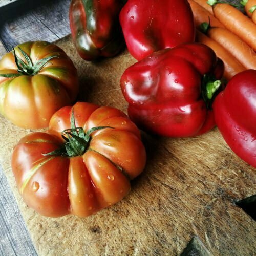 Fresh tomatoes and red peppers sit on a rustic chopping board. All ingreients are part. of the Mediterranean diet