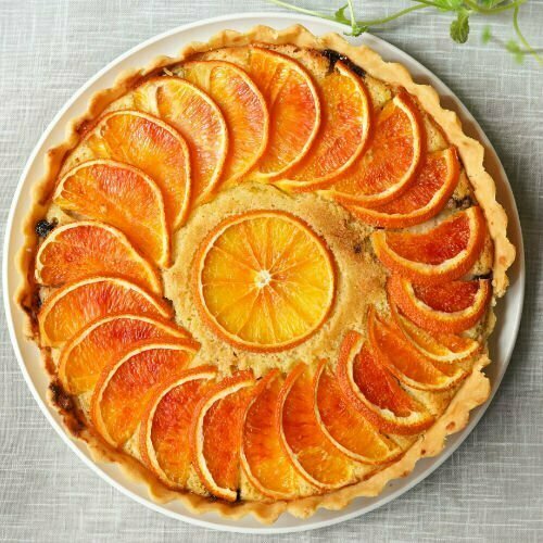 an orange cake is decorated with thin slices of orange placed symetrically around the cake