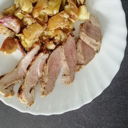 A plate of Spanish pork shoulder slices sits beside some roasted potatoes and garlic