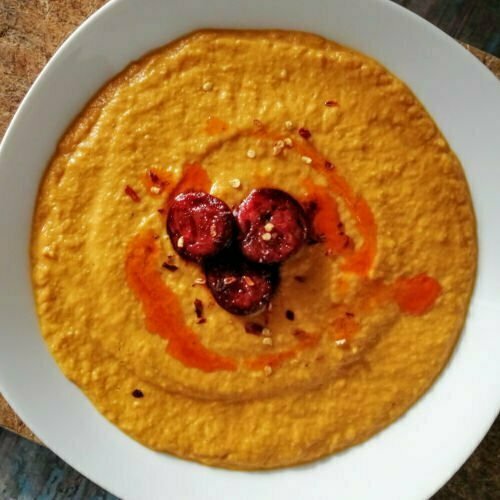 A white bowl contains pumpkin soup topped with some chorizo.