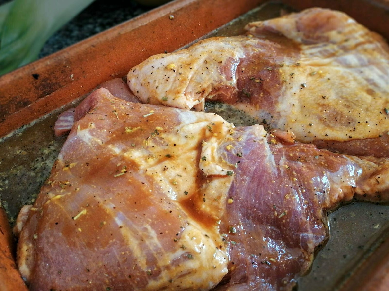 marinaded pork shoulders sit in an earthenware dish