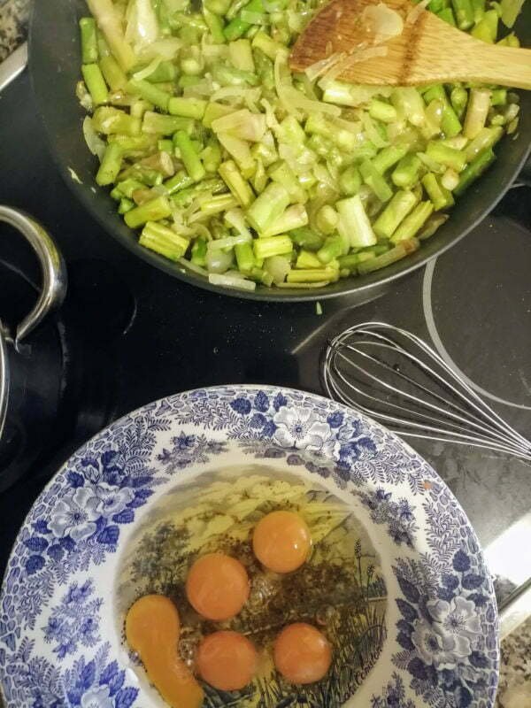 cooked asparagus. sits in a frying pan, a bowl of eggs sits to one side.