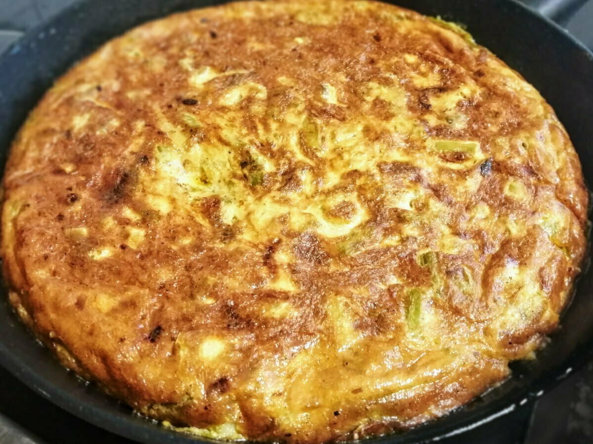 A alrge asparagus tortilla sits on a frying pan