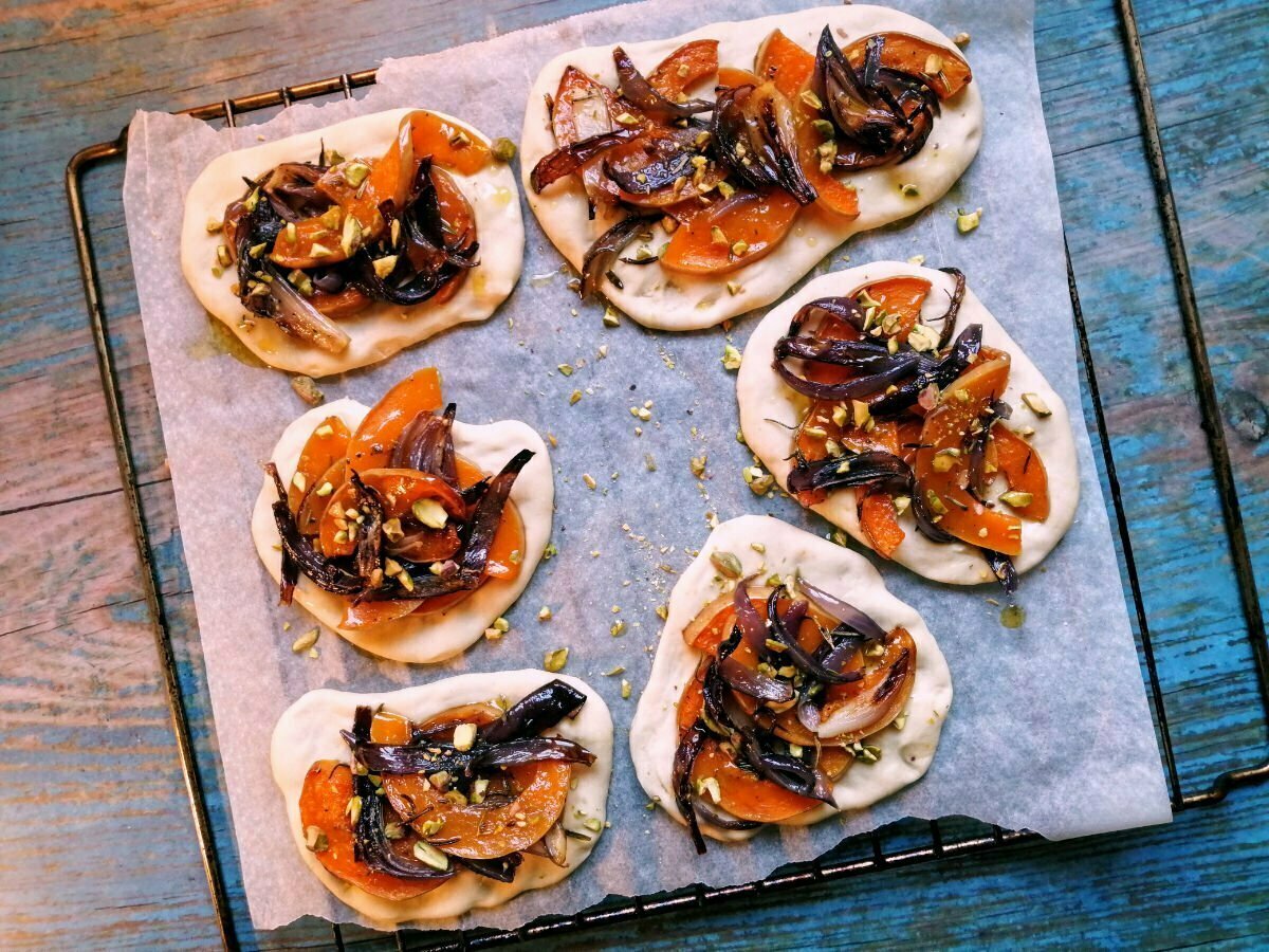 6 pumpkin and caramelized onion cocas sit on a baking tray with a rustic blue background