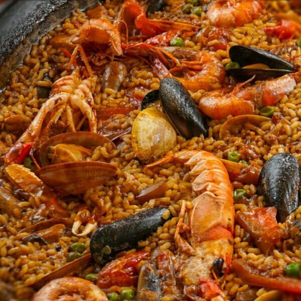 A large Seafood paella sits in a pan topped with clams, mussels, rings of squid, and large red shrimp