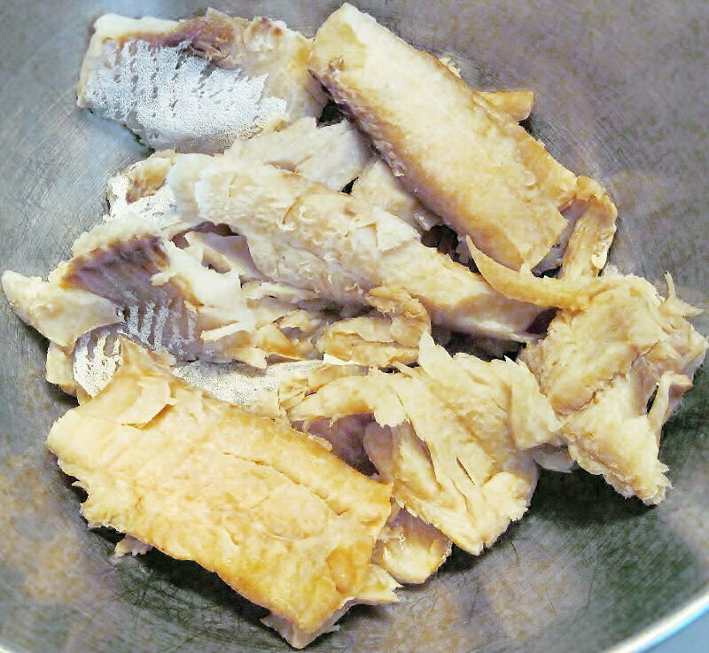 flakes of salted cod fish sit in a stainless steel bowl