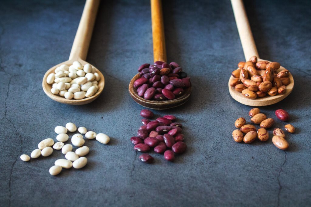 3 wooden spoons are topped with butter beans, black beans, and kidney beans.