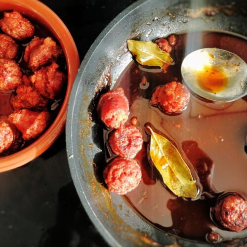 A fryig pan of chorizo cooked in cider sits beside an earthenware tapas dish filled with chorizo