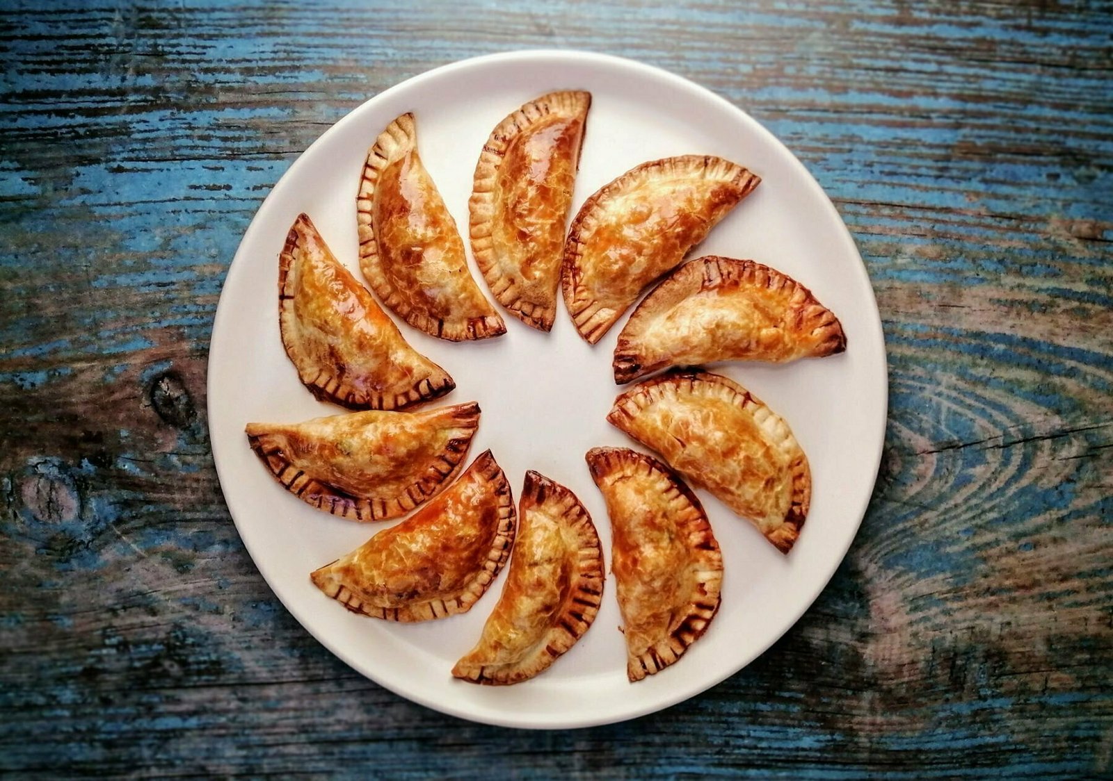a plate of chicken with cider infused chorizo empanadas sits arranged in a ring on a blue wooden board