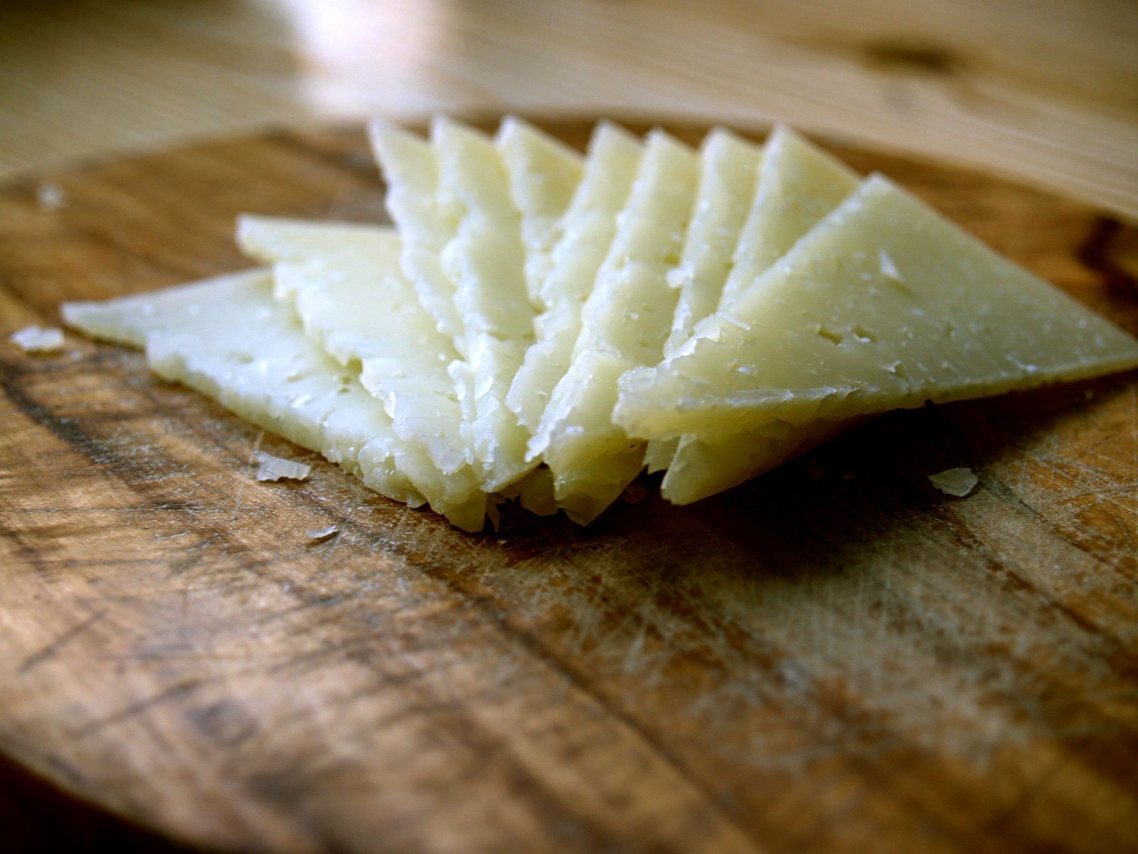 A few slices of manchego cheese sits on a rustic wooden chopping board