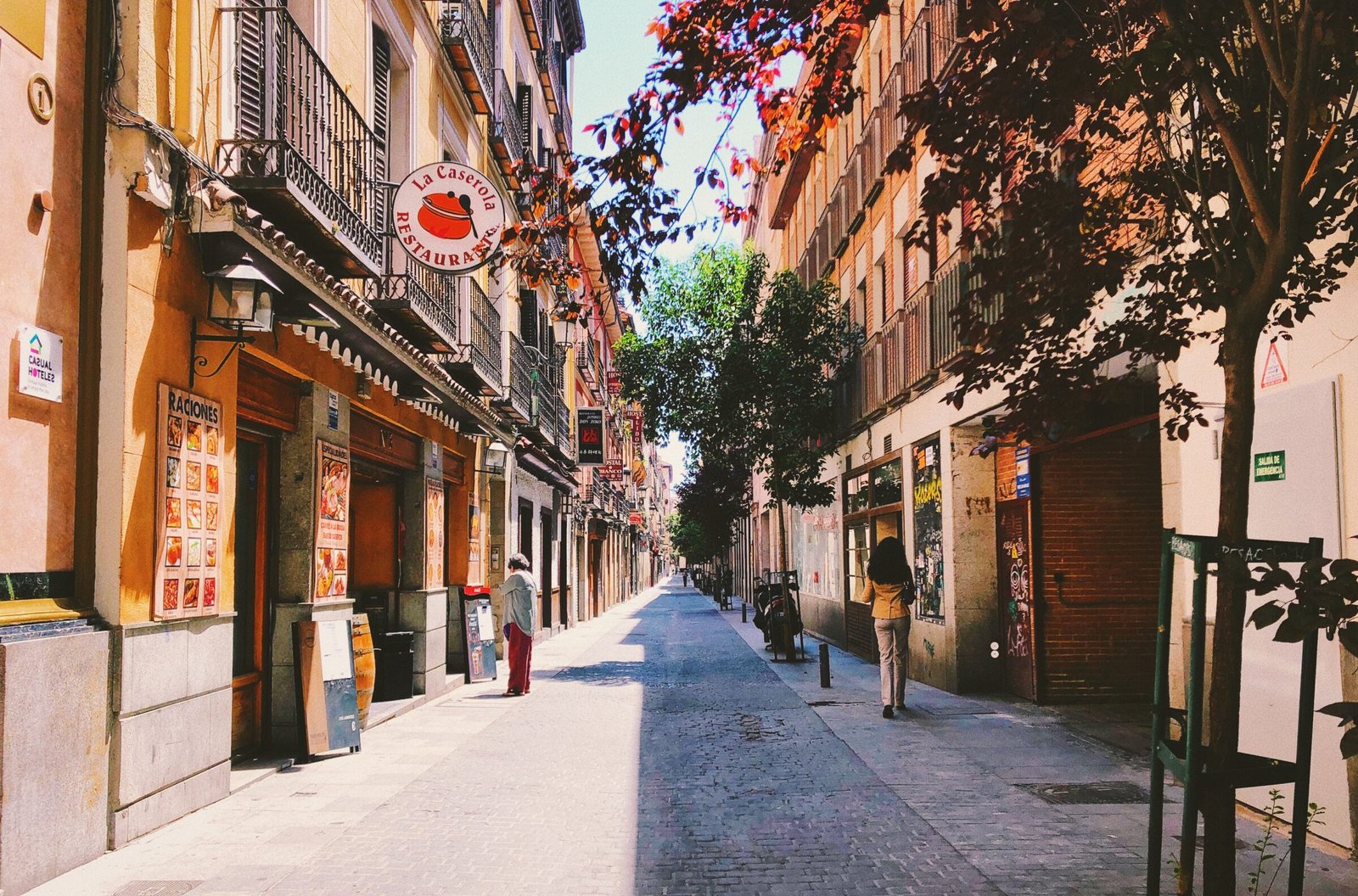 A street scene of Madrid showing small bars and shops along a tree lined cobbled street