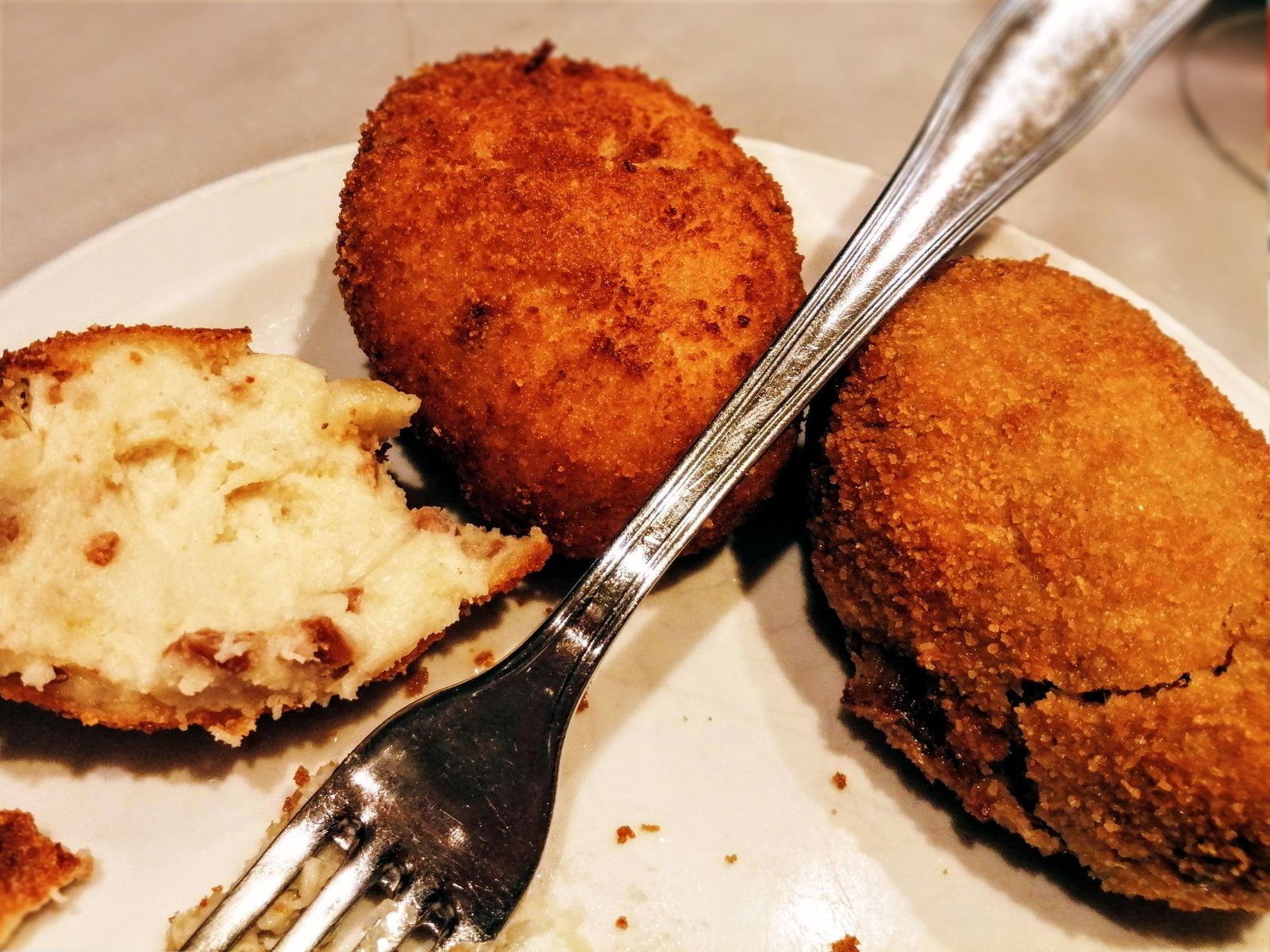 A few golden deep-fried croquettas sit on a plate with a fork