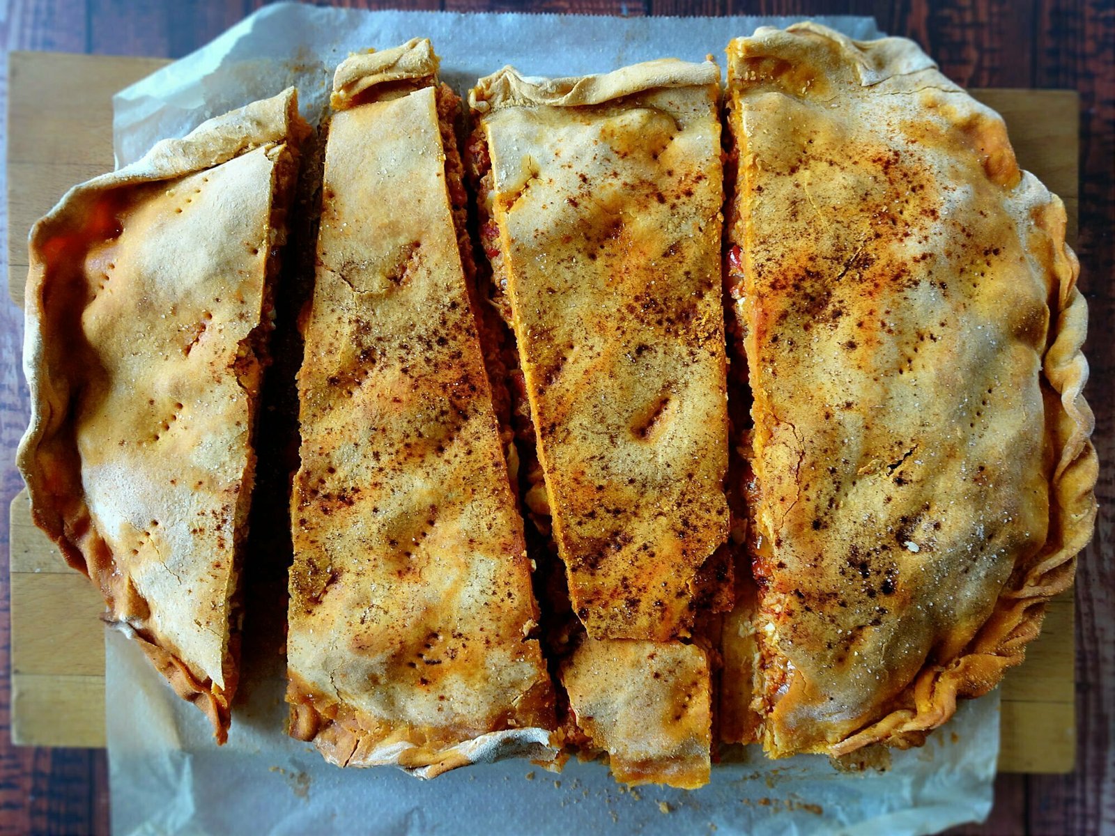 A large empanada gallega sits cut up into peices on some parchment paper