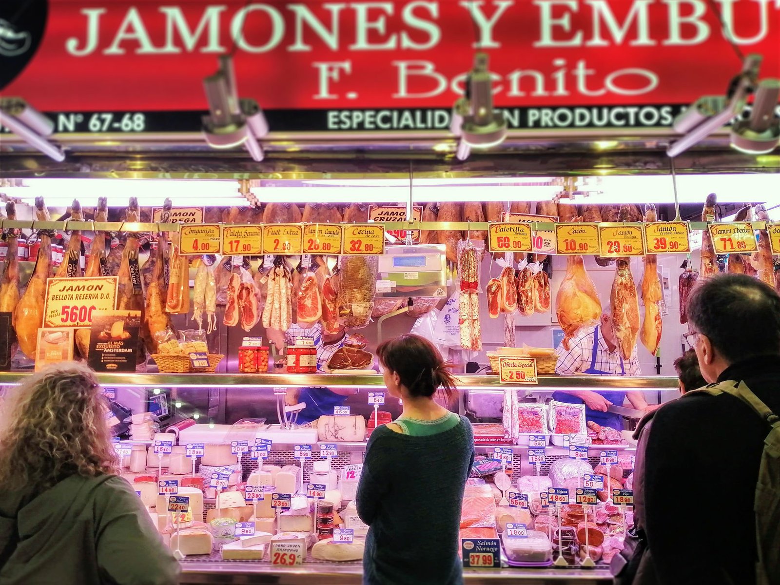 Customers wait at a meat counter in a busy market of Madrid