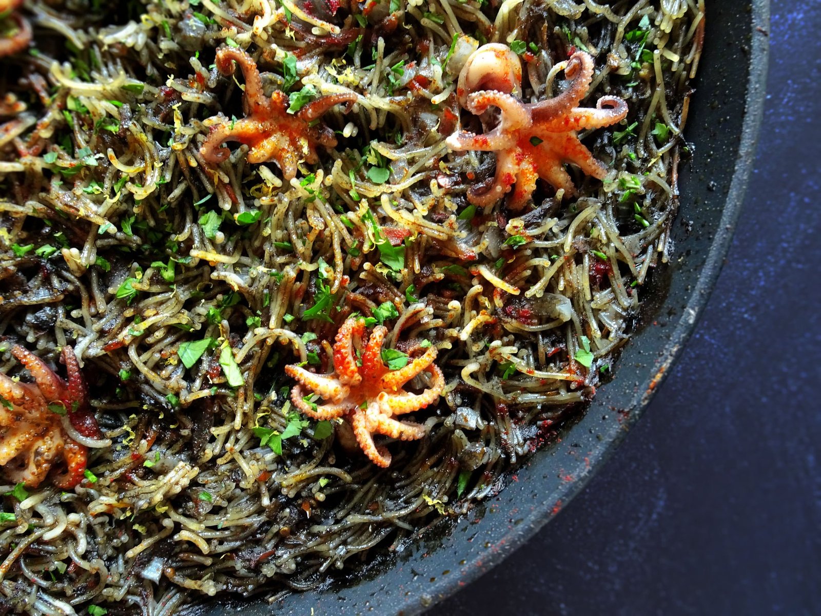 a close up photo of a pan full of fideua negra with baby squid sitting on top