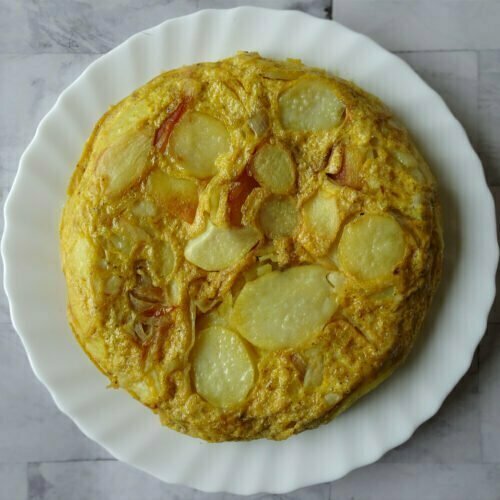 A large tortilla espanola sits on a WHITE PLATE ON TOP OF A GREY MARBLE COUNTERTOP