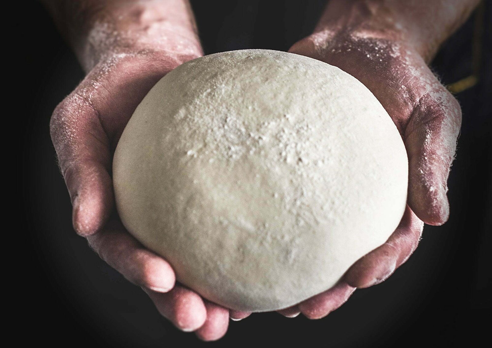 A large ball of dough is held by a bakers hands