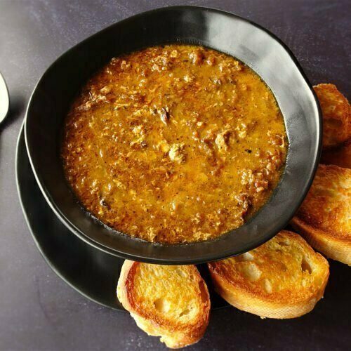 A black bowl full of garlic soup sits on a countertop beside a few slices of toasted bread