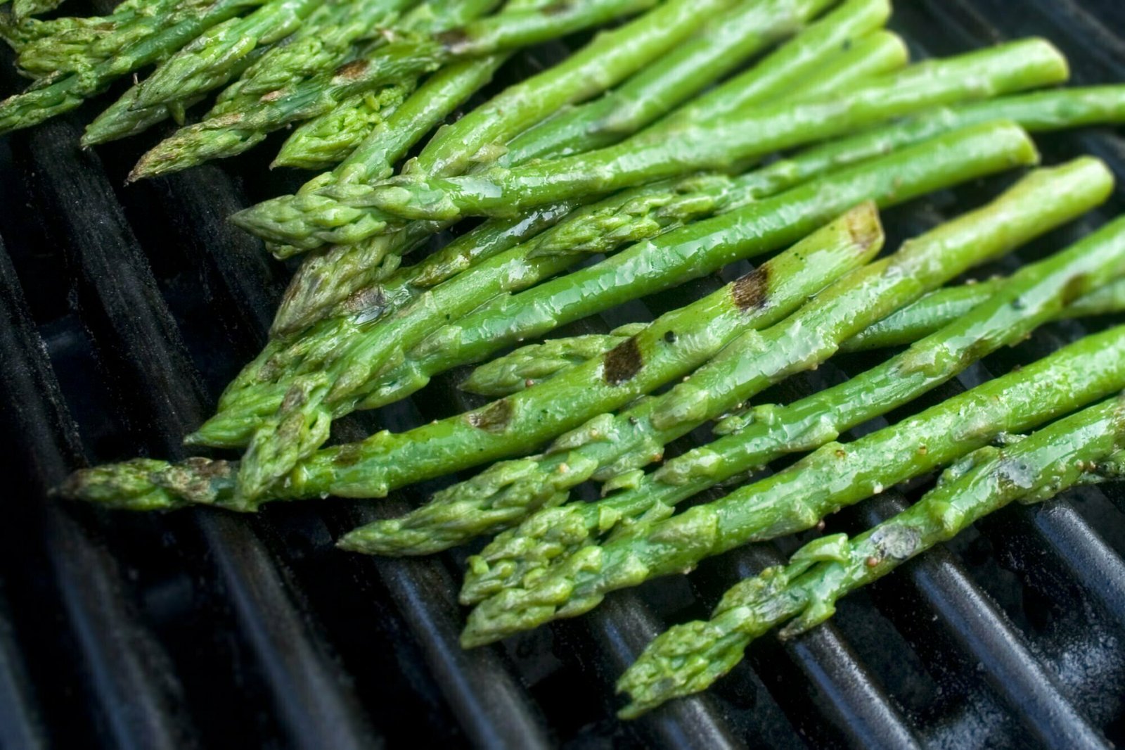 Some stems of green asparagus sits on a bbq grill