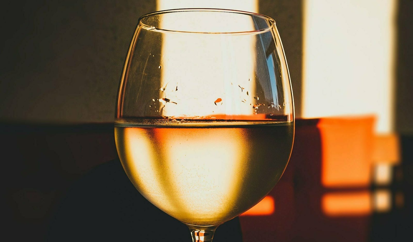a close up photo of a glass of white wine  sits with a blurred red background at sunset. 