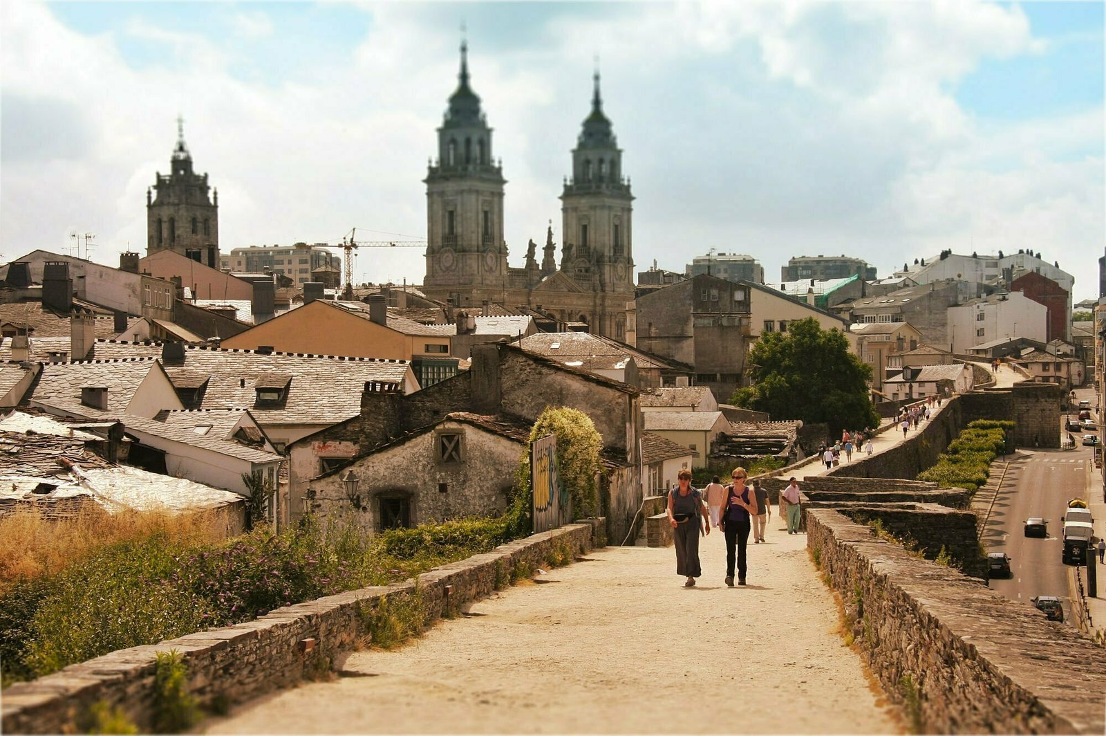 The roamn walled city of Lugo sits in the back ground with 2 spires rising into a blue sky from the cities cathedral.