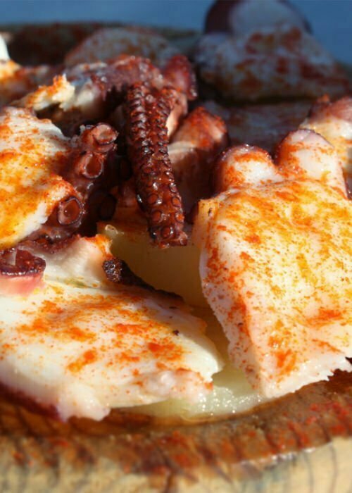 Some octopus garnished with paprika sit on a bed of potato scallops