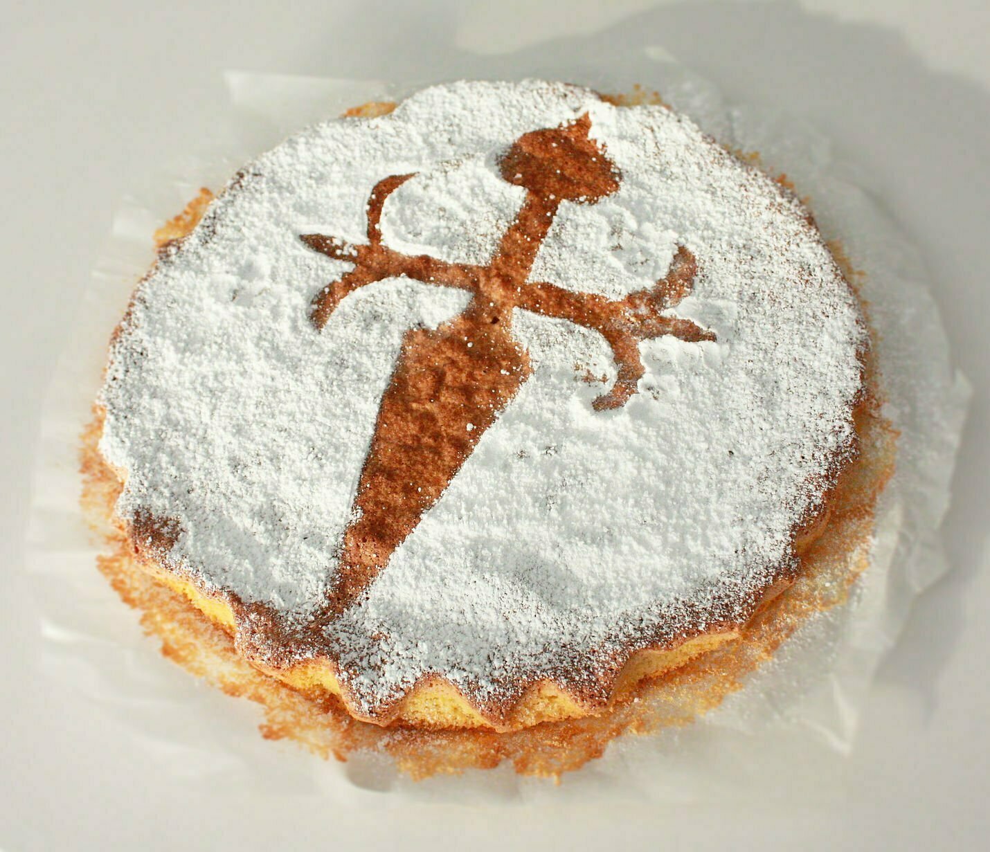 a tarte sits on baking paper with a symbol of Santiago cross made with icing sugar. 
