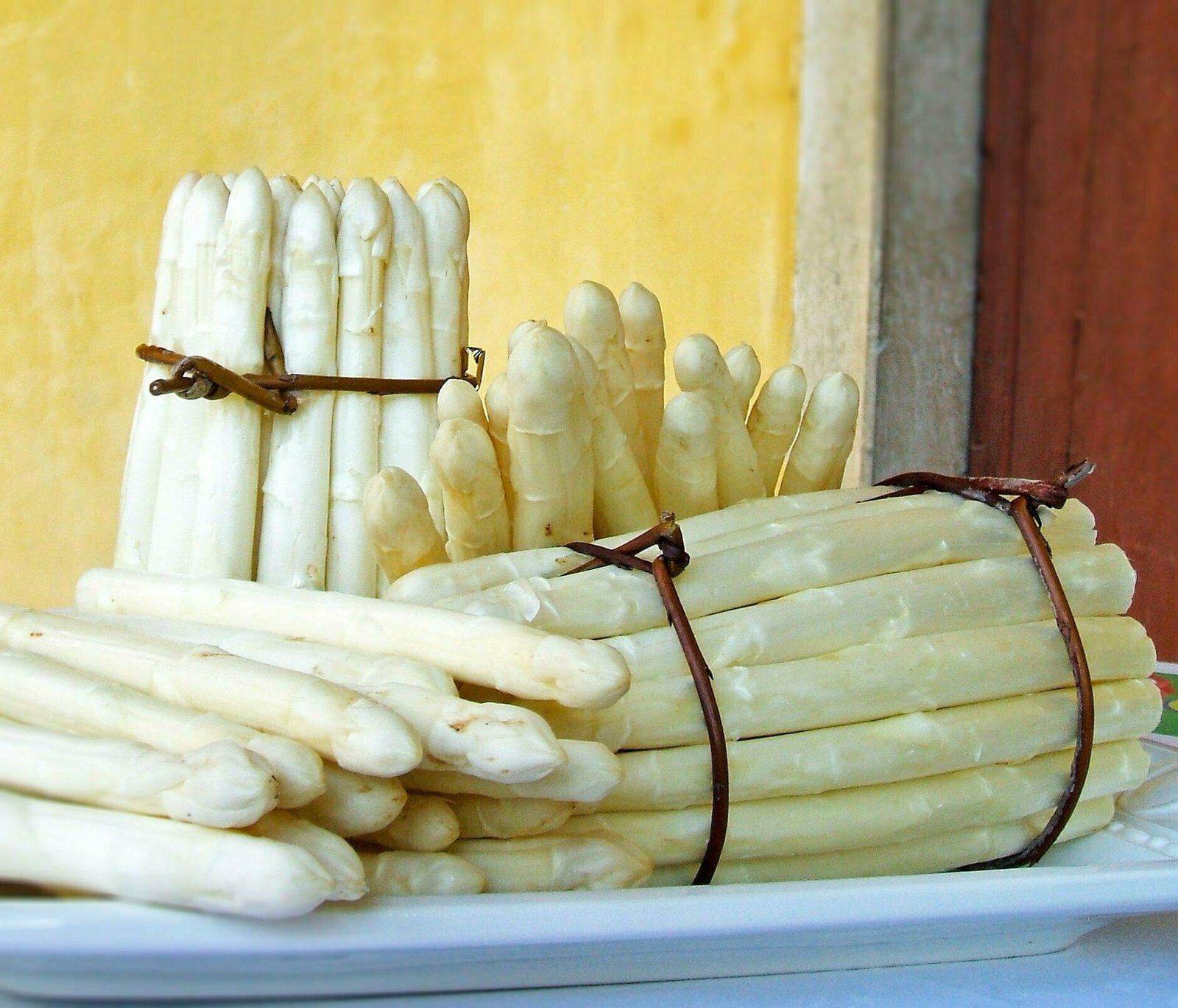 3 large bunches of white asparagus stalks sits on a counter.