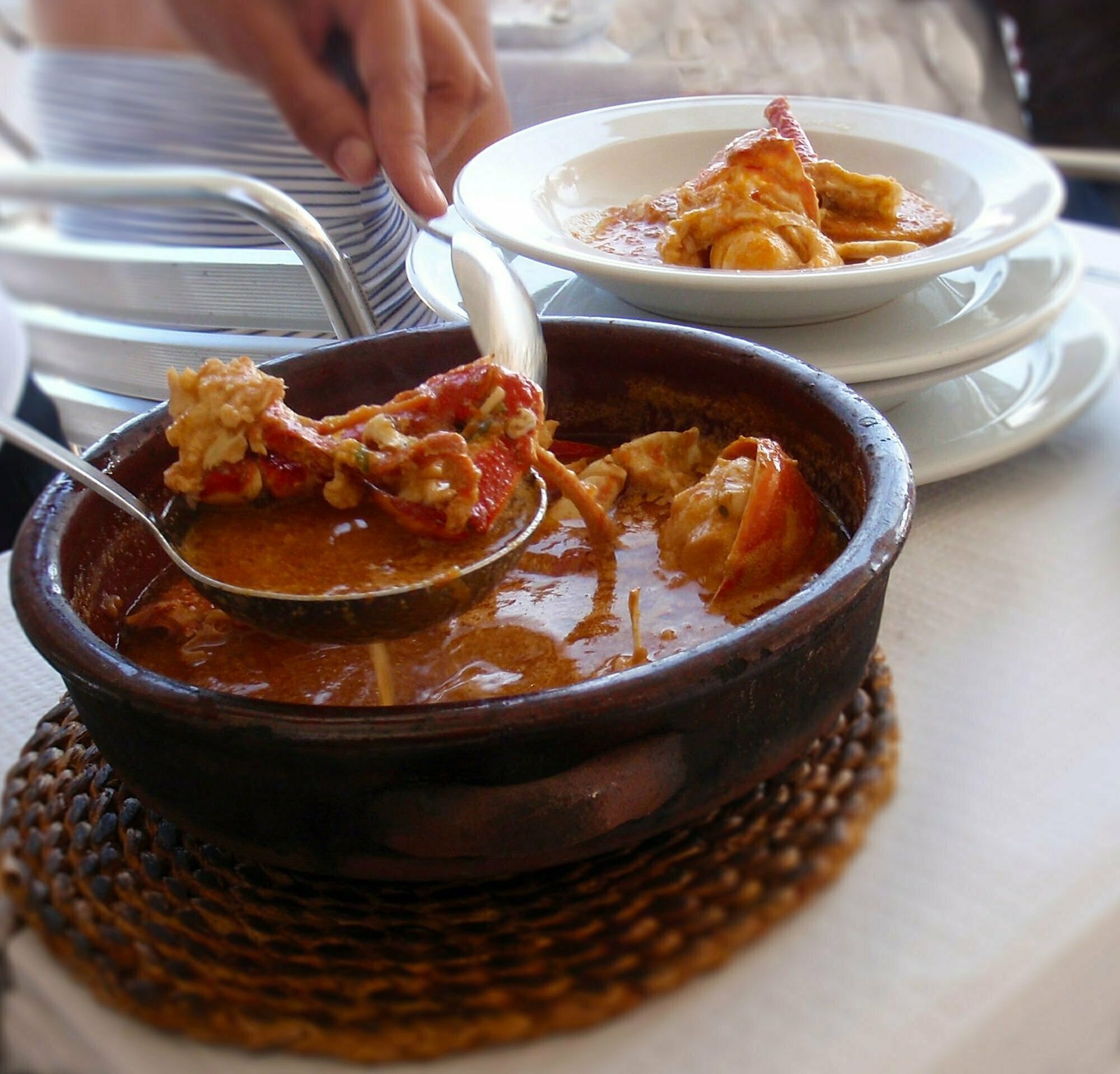 A table hold s a large bowl of Caldereta de langosta, a traditional Mallorcan dish thqt being served to guests in the background 