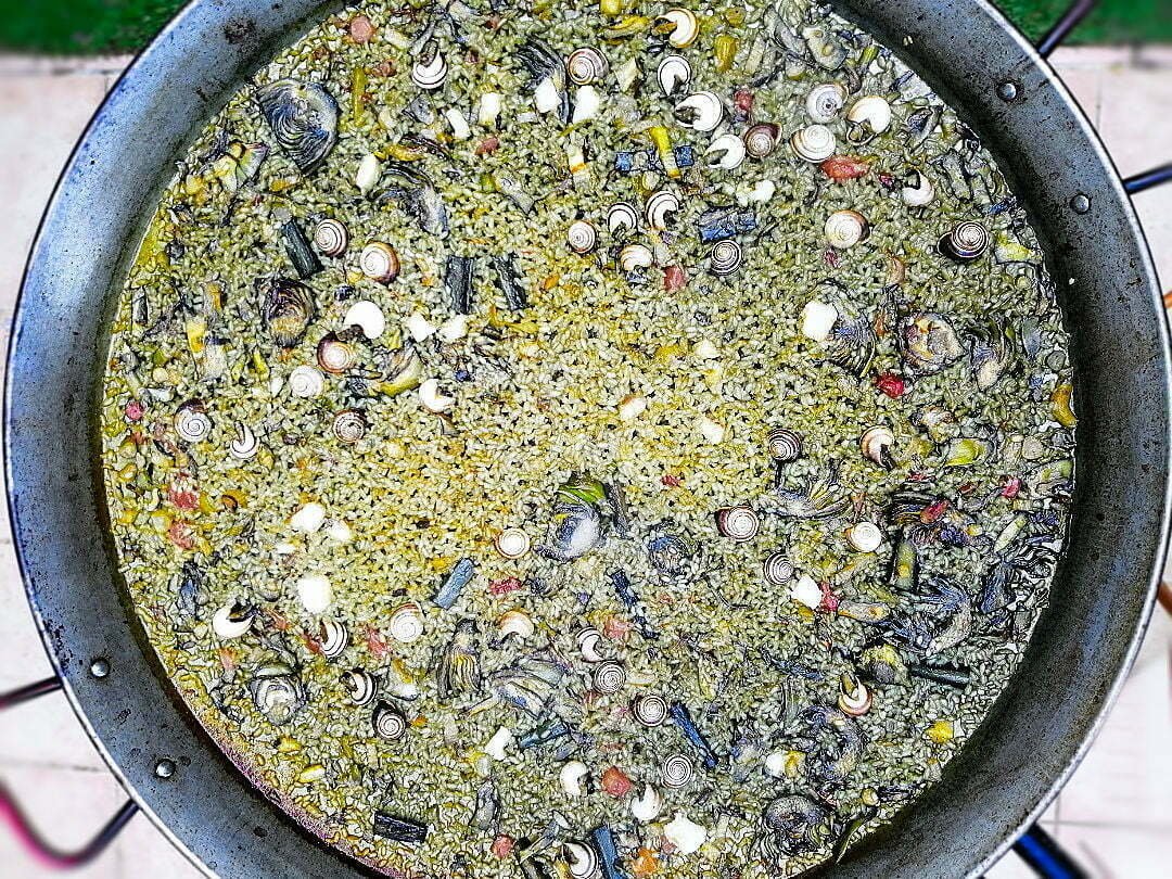 A large paella pan is cooking and Orchard paella with some vegetables and snails. 