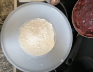 Flour and baking powder are sieved into a large white bowl
