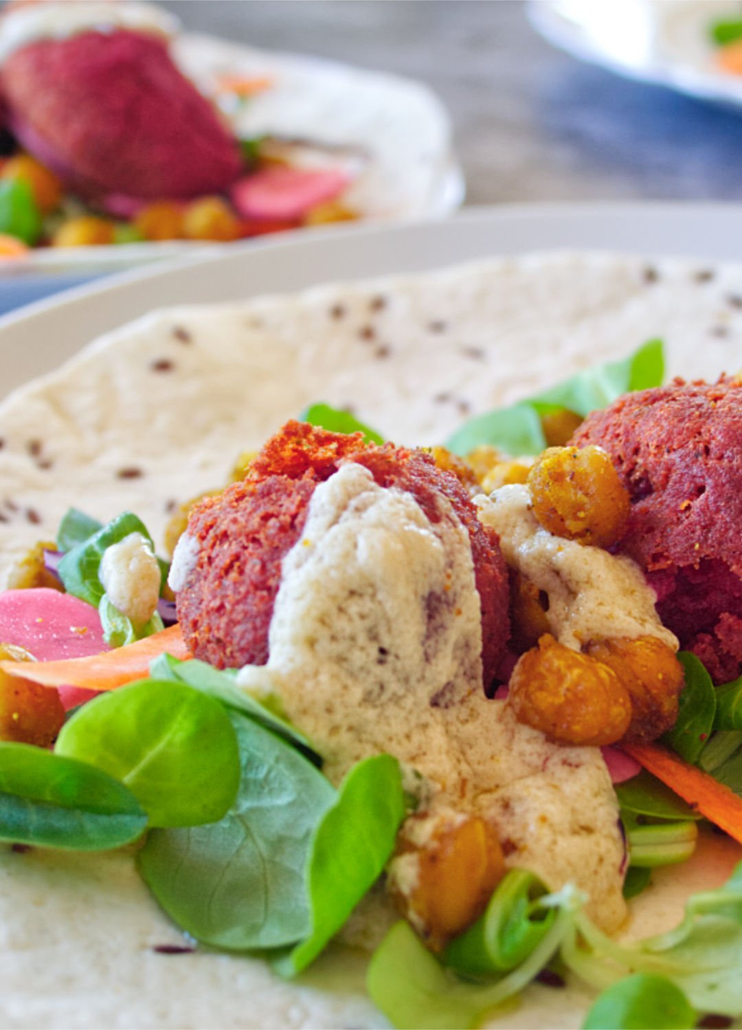 Beetroot falafels sit on a turkish wrap with some salad and topped with a few blobs of tahini sauce