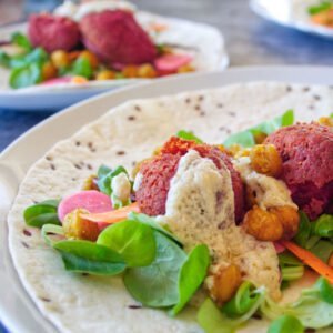 Beetroot falafels sit on a turkish wrap with some salad and topped with a few blobs of tahini sauce