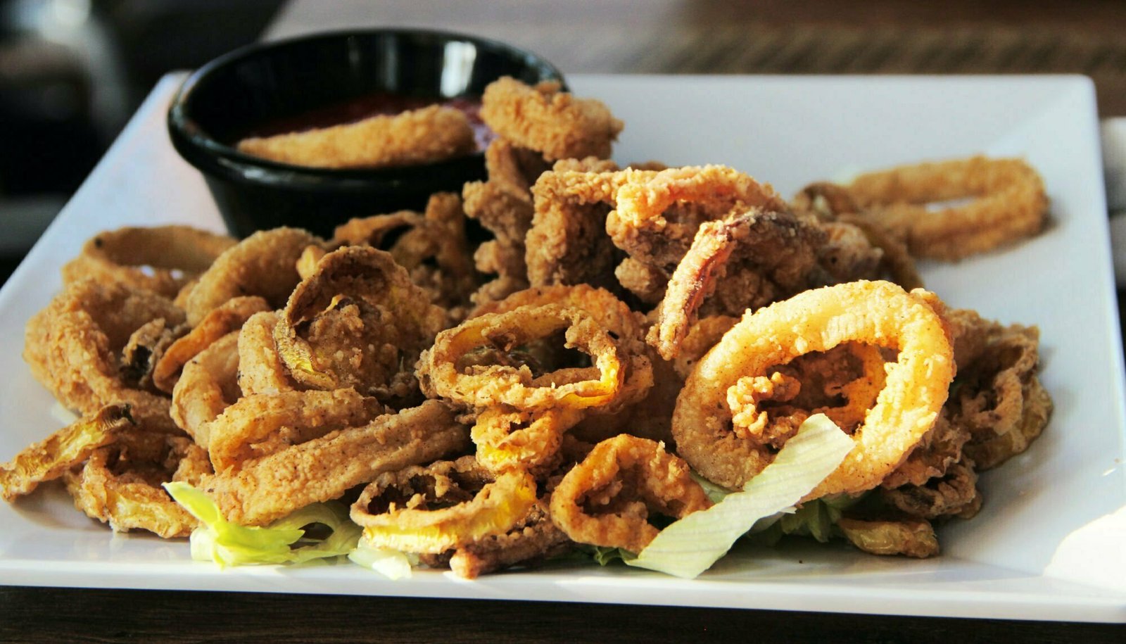 A large square plate sits filled with fried golden calamari