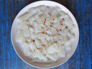 layers of ceviche are laid out on a white plate and sprinkled with chopped red chili