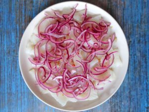 slices of white fish sit. topped with red onion and lime juice