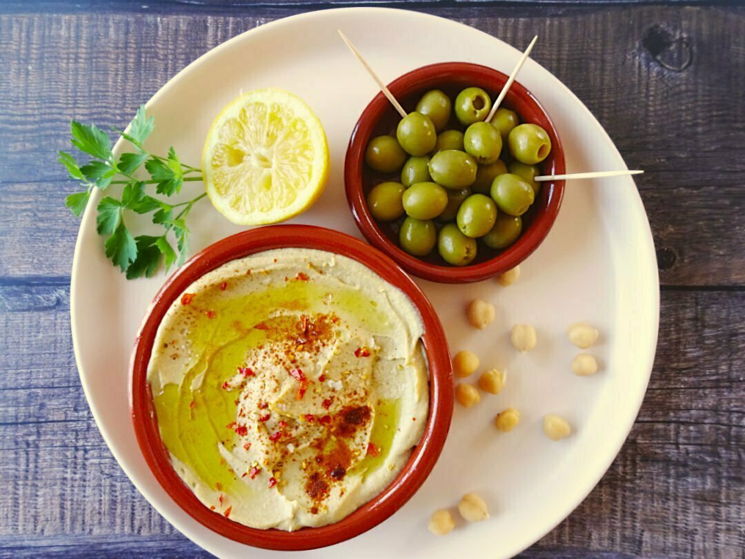A platter sits with some Mediterranean Hummus, green olives, lemon, and parsley