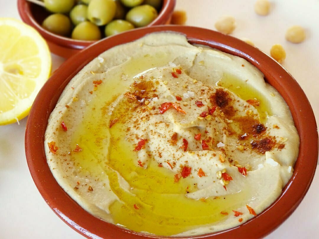 An earthenware bowl sits filled with Mediterranean hummus that's is topped with olive oil and some paprika