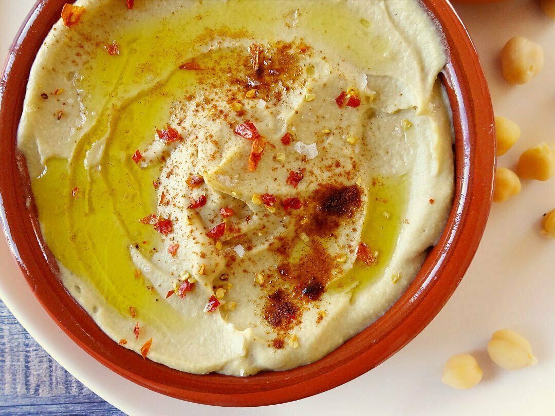 An earthenware bowl sits filled with Mediterranean hummus that's is topped with olive oil and some paprika